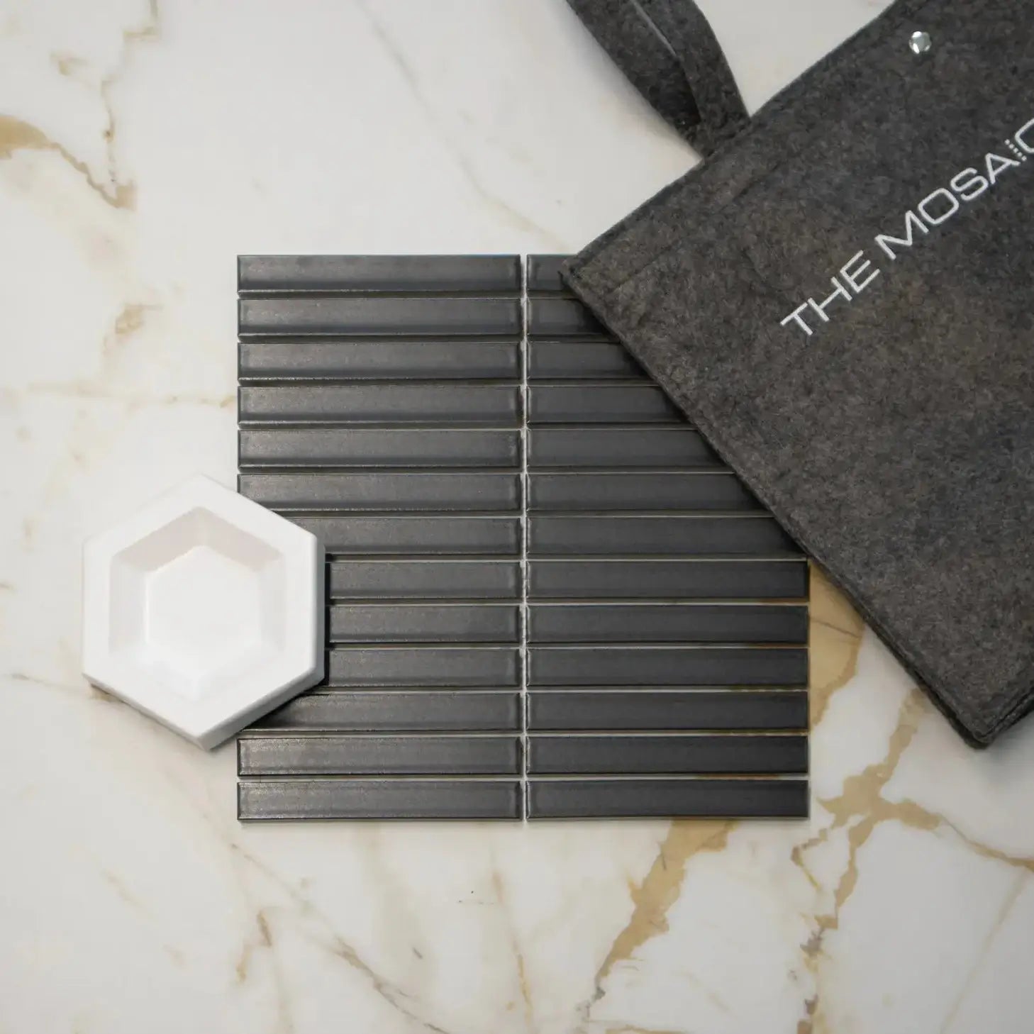 The Sevilla Mosaic Tiles, in a Carbon Shade Matt Black, with a size of 20x145mm resting on a light colored marble background.