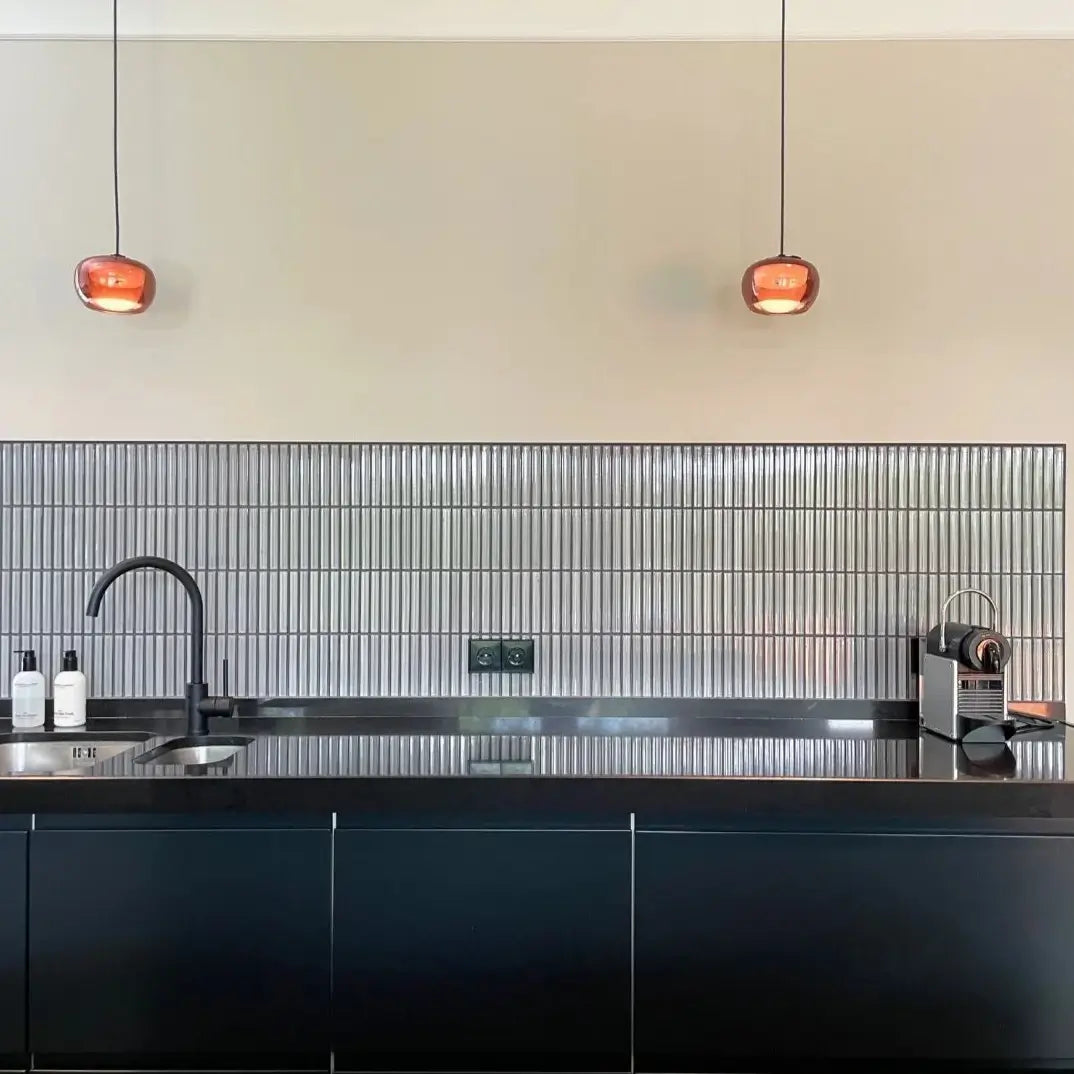 The Sevilla Mosaic Tiles, Original KitKat design in a Light Gray, with a size of 20x145mm installed on a kitchen wall with cabinetry in front, a basin sink and faucet and various kitchen supplies and equipment.