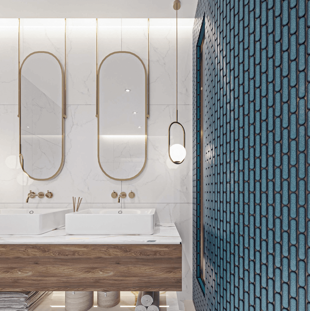 The Sevilla Mosaic Tiles, Oval design in Azure Blue, with a size of 23x98mm. Installed on a curved wall shower area within a bathroom. A vanity with a double sink basin set up with two mirrors mounted above to the left.